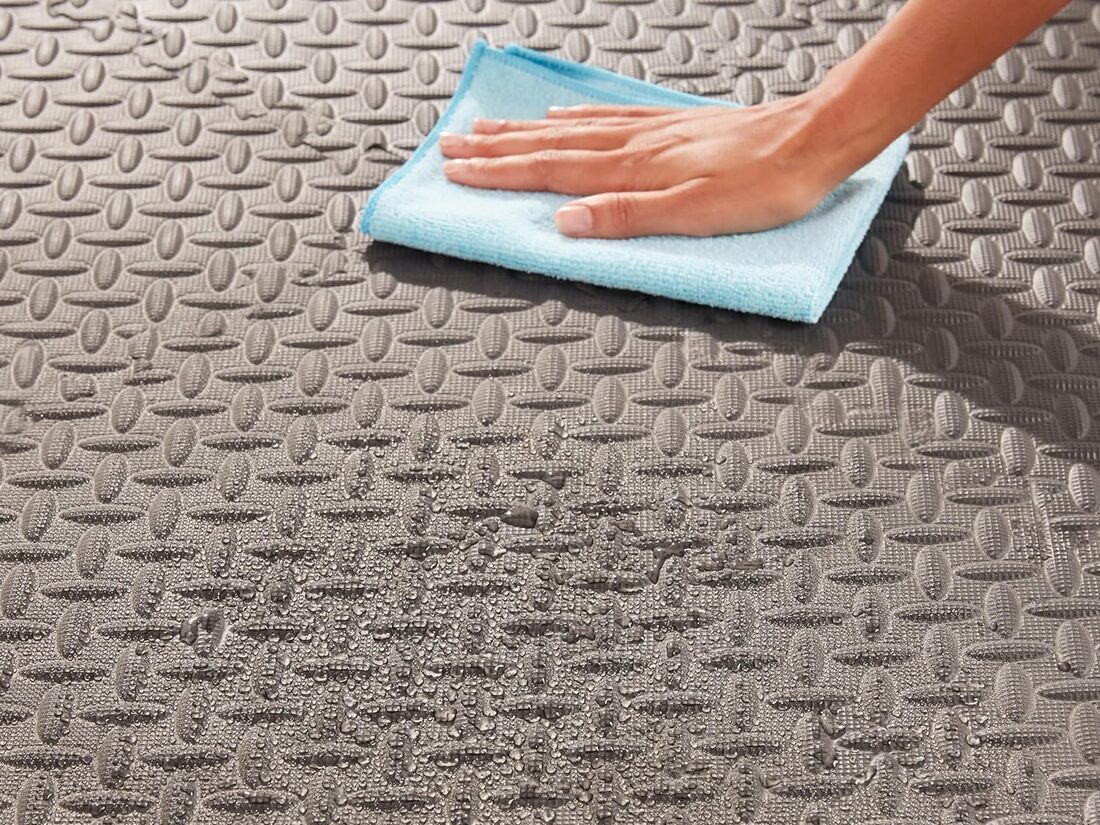 A person in a home gym space carefully wiping down EVA foam floor tiles with a damp cloth