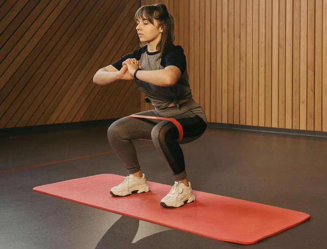  A woman performs resistance band squats, engaging her quads, glutes, and hamstrings