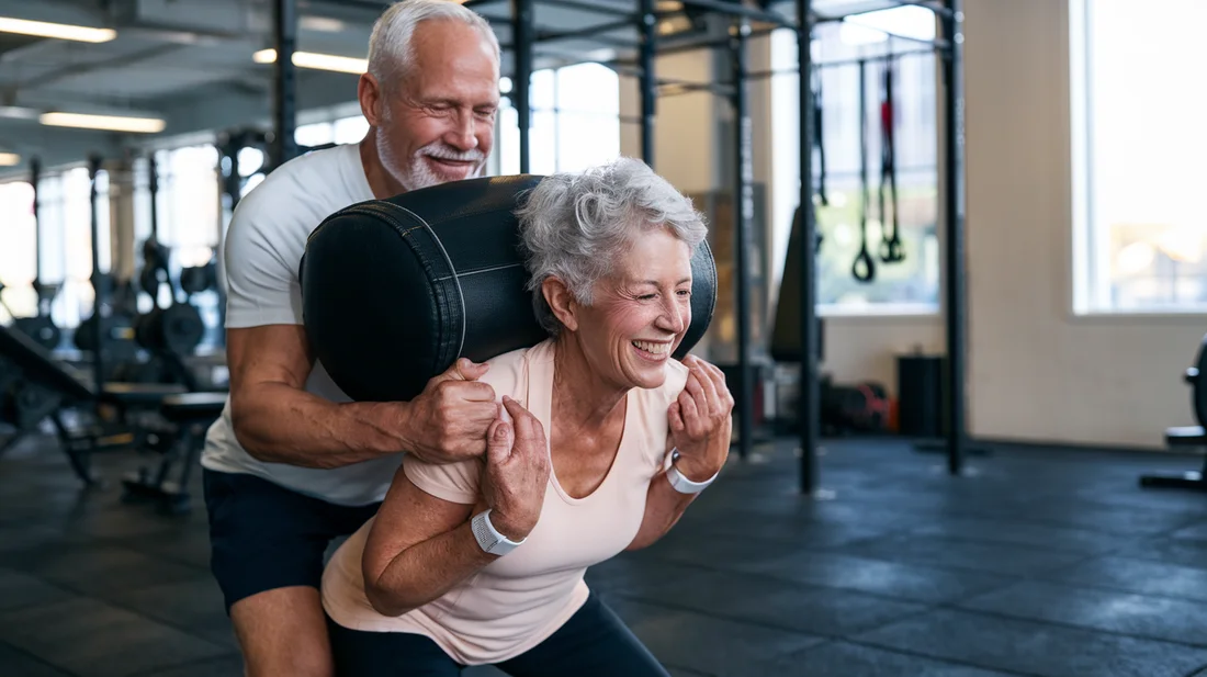 A smiling senior couple performing a sandbag squat together