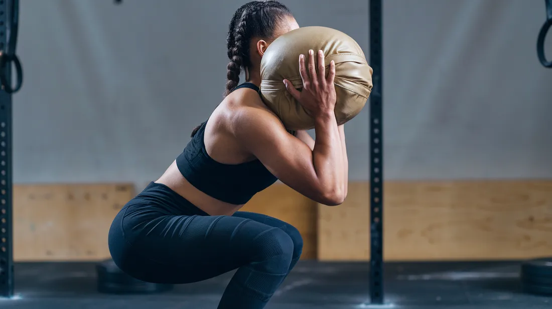 A side view of a person demonstrating the proper form for a sandbag squat, with their back straight, knees over toes and core engaged