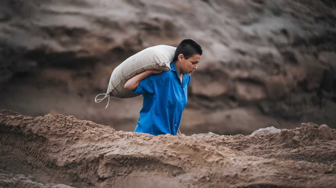 Person carrying a sandbag on a rocky trail, illustrating how sandbag training improves balance for uneven hiking paths