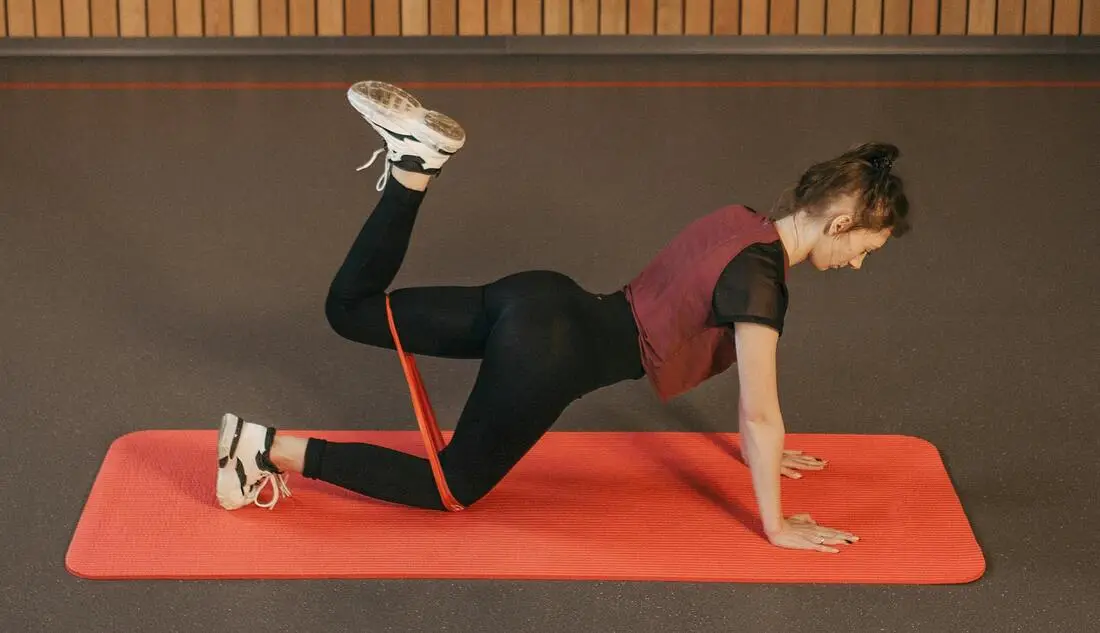 A woman on all fours performs fire hydrant exercises with a resistance band