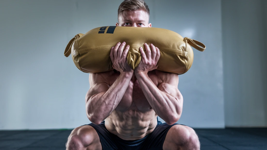 A man doing a squat exercise with a sandbag 