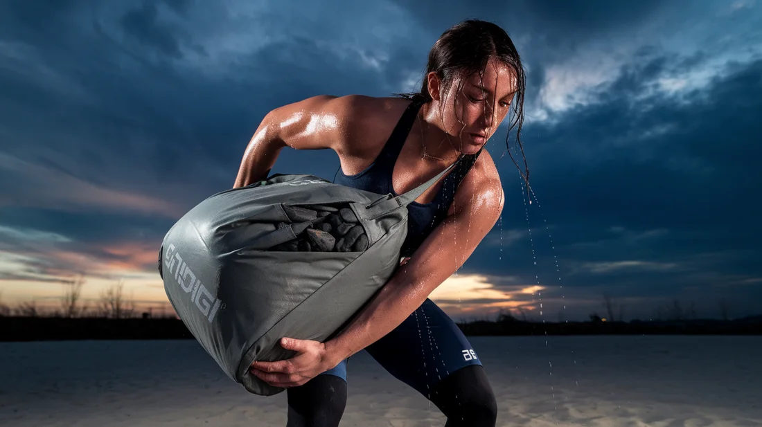 A person performing a sandbag clean and jerk exercise against a dramatic sky background